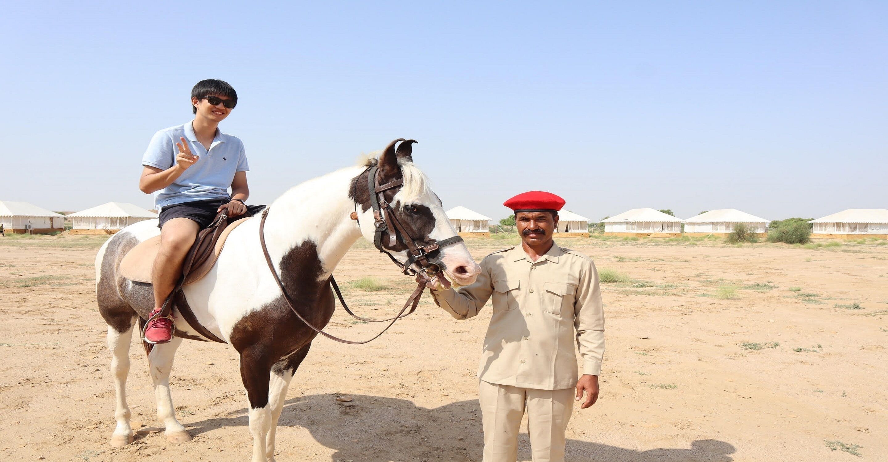 A person on a horse in a desert setting with tents in the background.