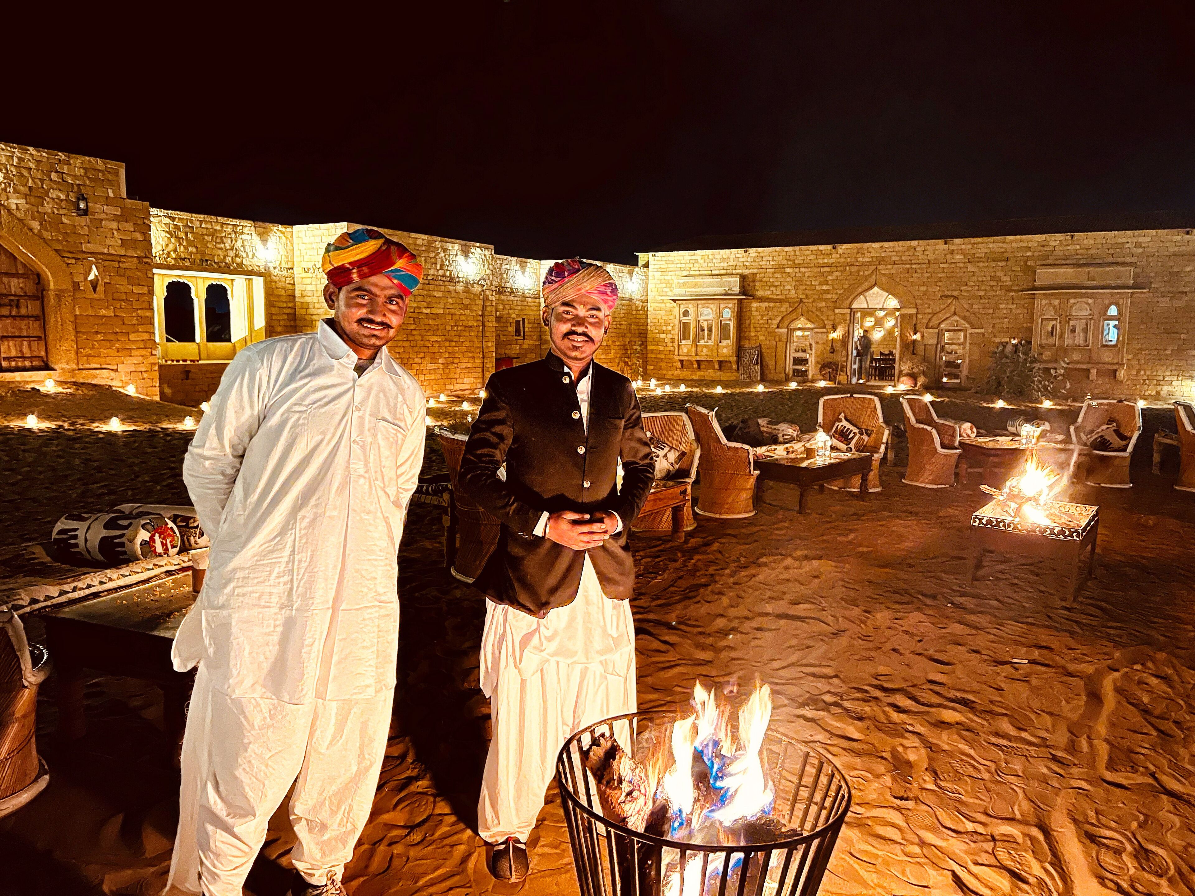 Two men standing in a courtyard with a fire pit and traditional seating.