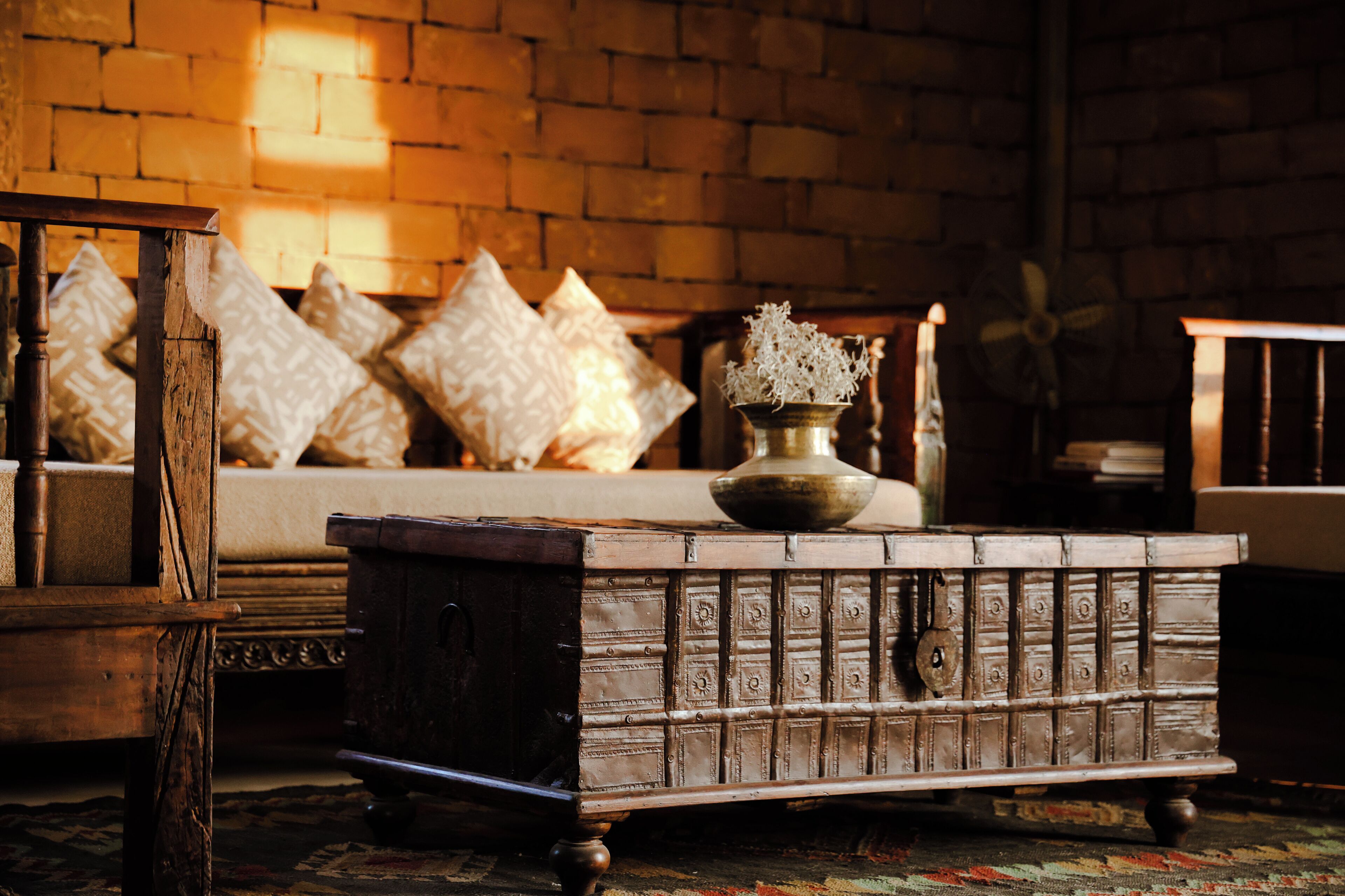 Une pièce comprenant un canapé, des coussins à motifs, un vase décoratif et une vieille commode.