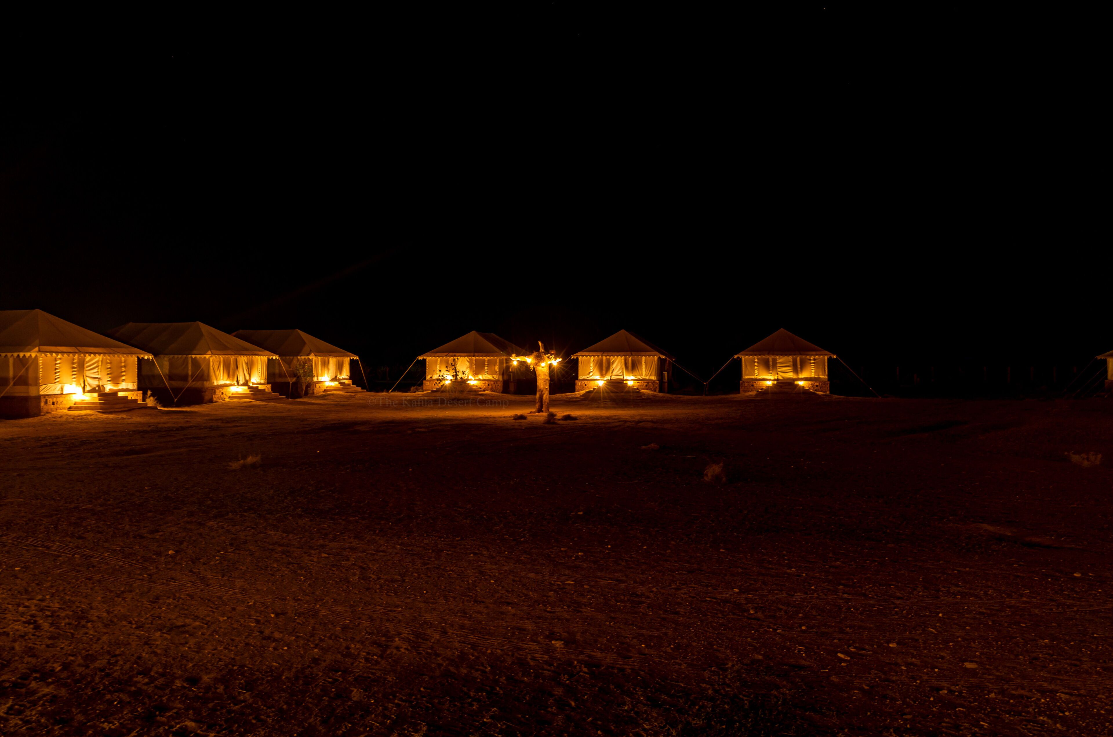 A row of tents with lights, set on a flat terrain at night.