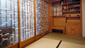 A traditional Japanese room with tatami flooring, sliding doors with floral patterns, and wooden furniture including a cabinet and shelves. - Inn-itiate Tainan (Tainan)