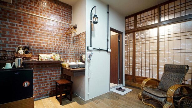 A compact living space with a brick wall, a small kitchen area, a traditional Japanese sliding door, and a wicker chair. - Inn-itiate Tainan (Tainan)