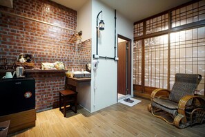 A compact living space with a brick wall, a small kitchen area, a traditional Japanese sliding door, and a wicker chair. - Inn-itiate Tainan (Tainan)