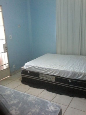 Een kamer met een bed, een matras op de vloer en een raam met zonwering.