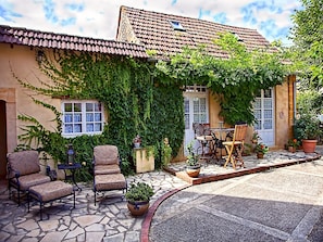 Ein Haus mit Ziegeldach, einer überdachten Terrasse mit Gartenmöbeln und einem Gartenbereich mit Blumentöpfen.