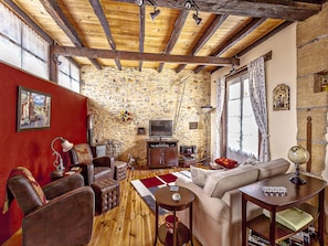 Ein gemütliches Wohnzimmer mit einer Steinwand, Holzbalken an der Decke, einem Fernseher und einer roten Akzentwand.