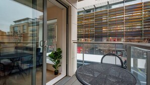 A modern outdoor seating area with a glass door entrance, a potted plant, and a metal table. - MySquare Apartments Shoredtich (London)