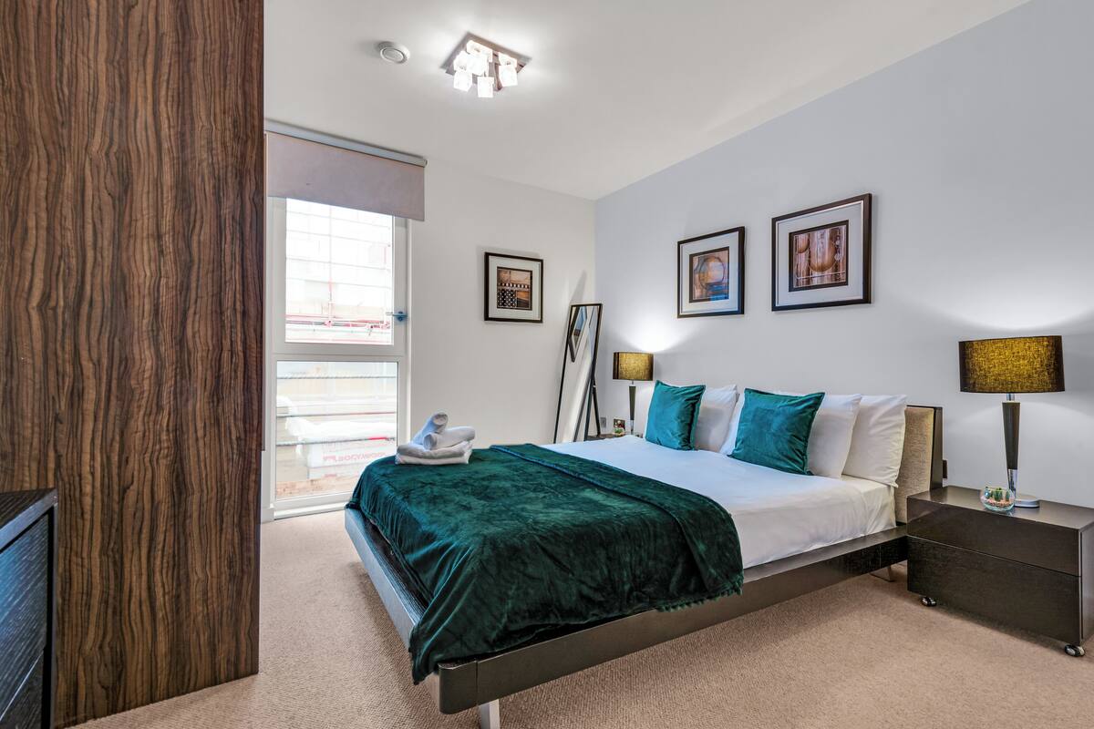 A modern hotel room with a large bed, a bedside table, a lamp, and framed pictures on the wall.