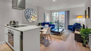 A modern apartment with a kitchen, dining area, and living room. It features a large window, a blue sofa, and a coffee table. - MySquare Apartments Shoredtich (London)