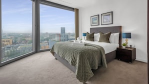 Un dormitorio moderno con un ventanal grande, una cama con una manta verde, dos mesitas de noche y cuadros enmarcados en la pared.