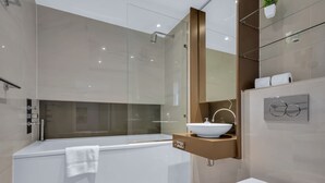 Un baño moderno con ducha de vidrio, una bañera blanca y un lavamanos blanco sobre encimera color beige.