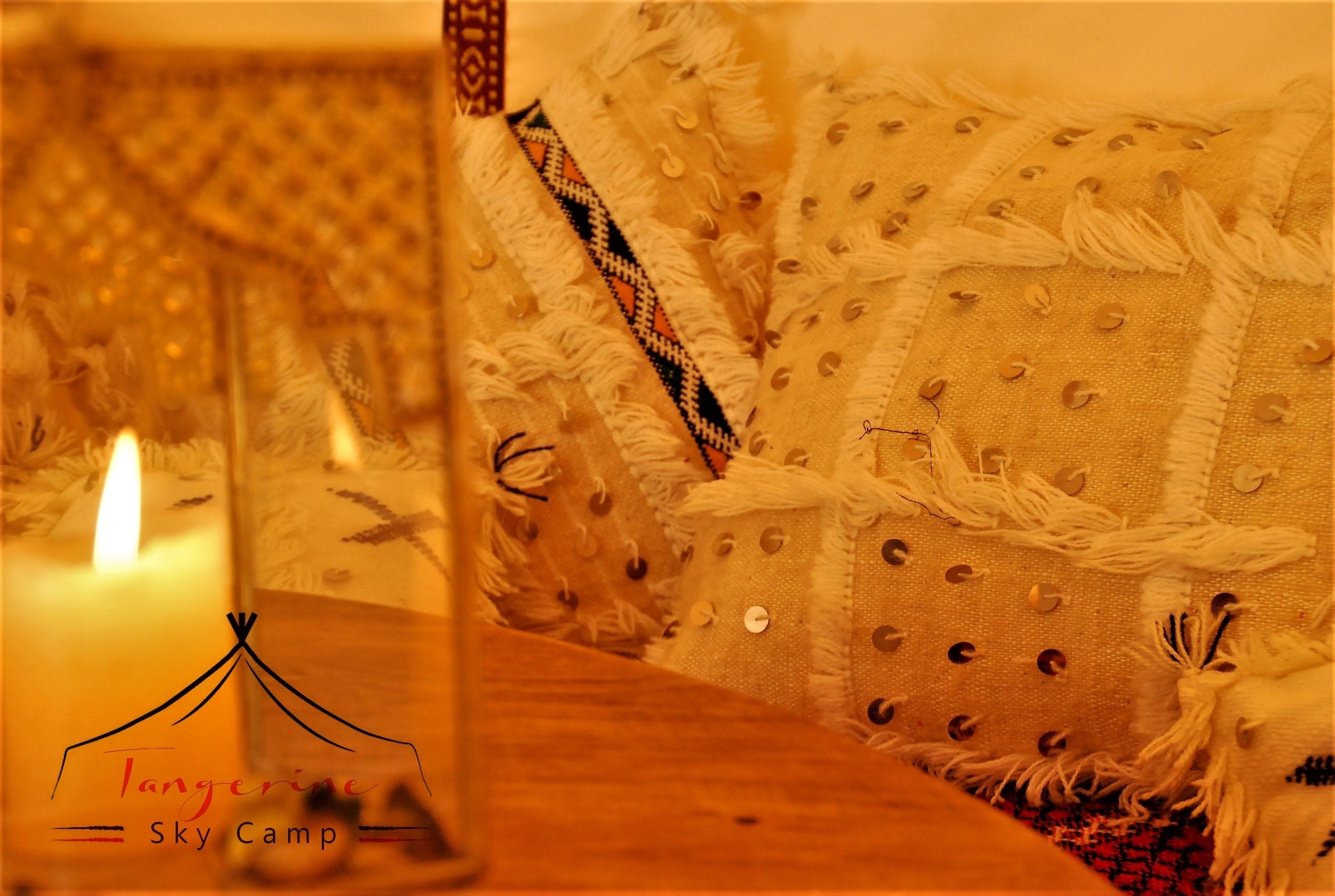Una habitación acogedora con una vela encendida, un tejido estampado y el logo de Tangerine Sky Camp.