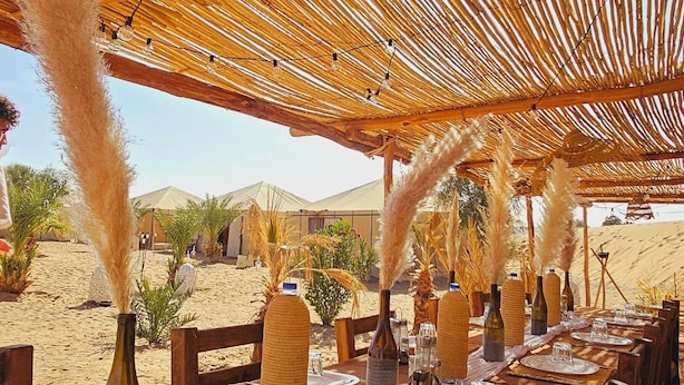 Un espacio de comedor al aire libre con techo de bambú y mesas preparadas para una comida, con vistas a un paisaje desértico.