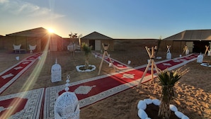 Un campamento en el desierto con tiendas de campaña, una alfombra roja y faroles decorativos.