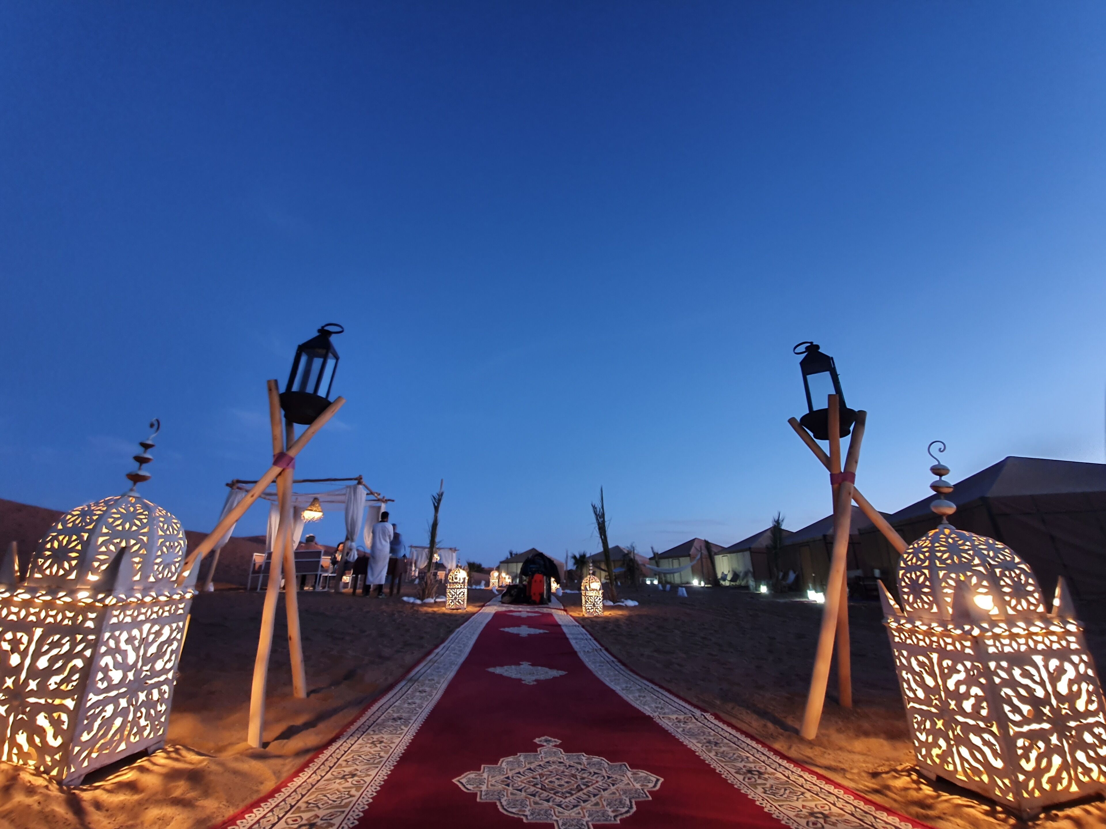 A carpeted pathway flanked by ornate lanterns leading to a building.