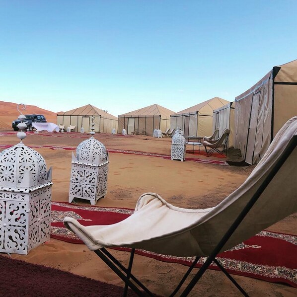 Un campamento en el desierto con tiendas, una silla de descanso y faroles decorativos.