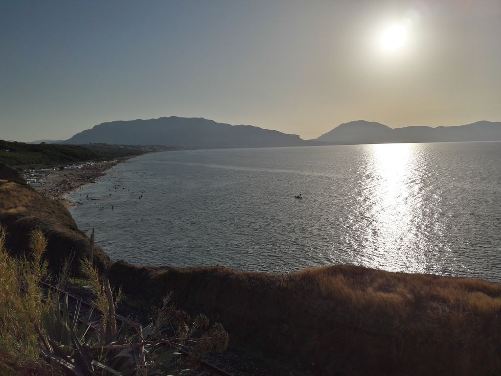 Un paisaje costero con cielo despejado, mar tranquilo y montañas a lo lejos.