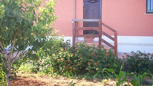 A building with a wooden staircase leading to a door, surrounded by flowering plants and a tree. - Blue Pools Relax Casa Martina (Balestrate)
