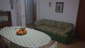 A dining area with a checkered tablecloth, a bowl of fruit, a sofa, and a door leading to another room.