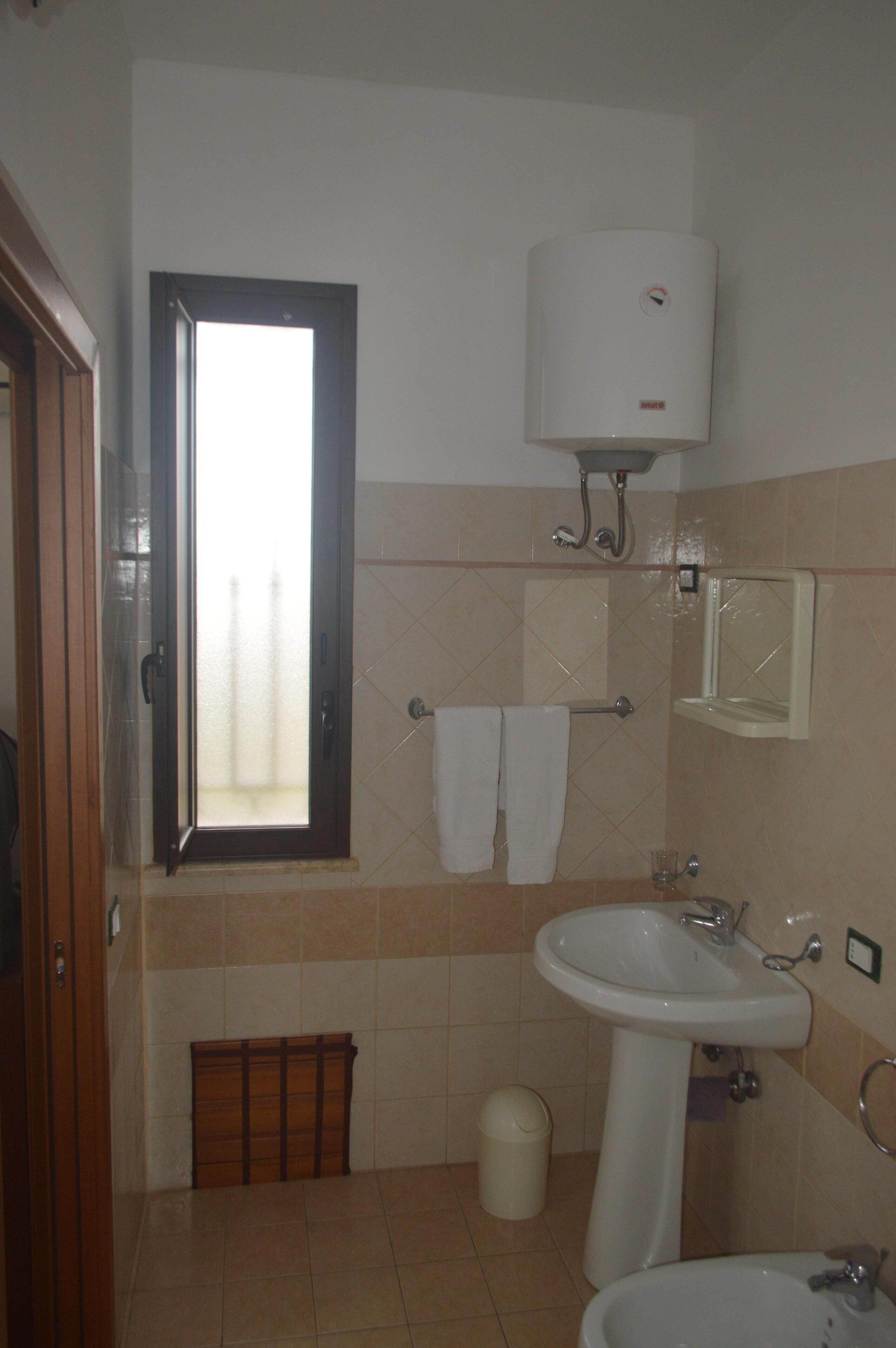 Casa de banho com janela, lavatório, espelho e porta-toalhas.