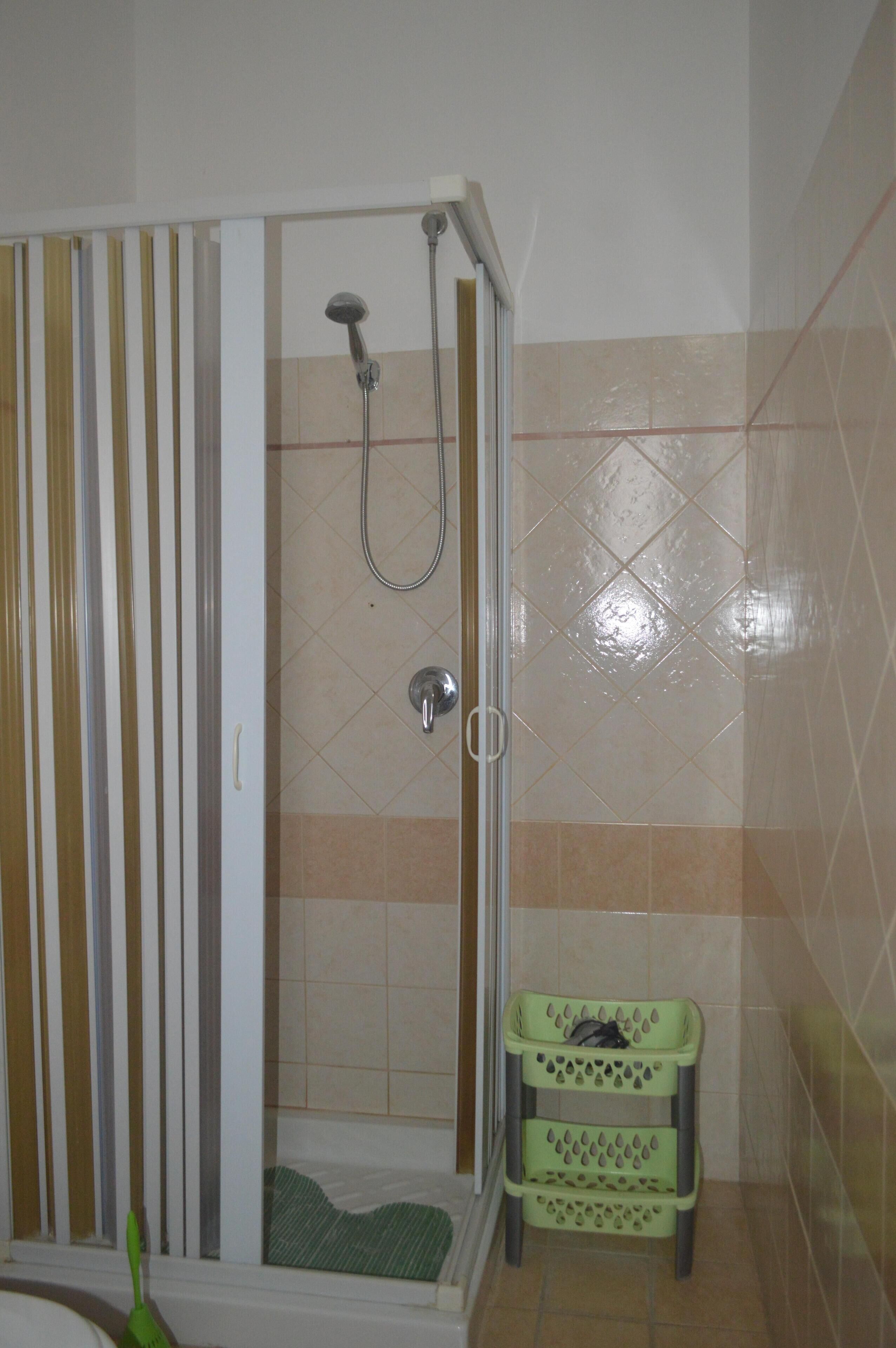 A shower area with a glass door, a showerhead, and a green plastic basket.