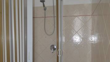 A shower area with a glass door, a showerhead, and a green plastic basket.