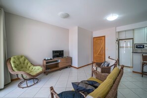 Una sala de estar con una silla tapizada de verde, un sofá de mimbre, un armario de madera y un televisor sobre un mueble.
