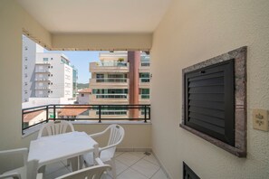 Un balcón con mesa y sillas, una ventana con vistas a otros edificios y un aire acondicionado de pared.