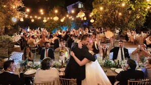A wedding reception with guests seated at tables, a couple dancing in the center, and string lights overhead.