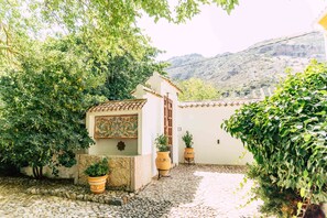 A courtyard with a tiled floor, potted plants, and a building with a tiled roof and a mural. - Cortijo Abril - Luxury Andalusian Finca for families, groups and celebrations (Priego de Córdoba)