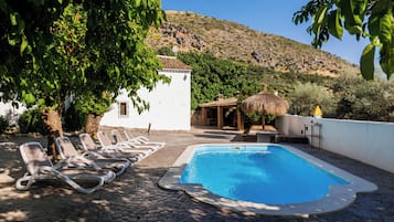 A swimming pool with lounge chairs, a white building, and a mountain in the background.