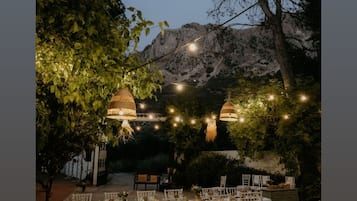 An outdoor dining area with round tables and chairs, string lights, and a mountainous backdrop.