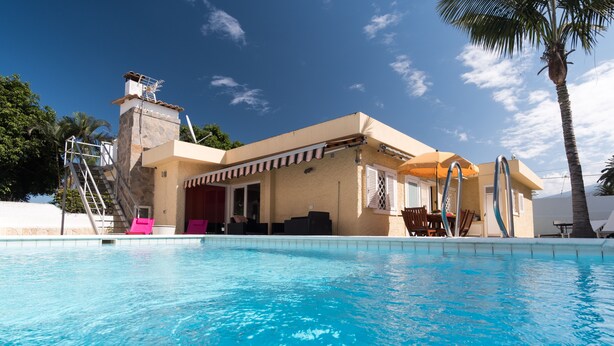 A swimming pool area with a stone staircase leading to a covered deck, surrounded by palm trees and a clear blue sky. - Taoro House, Puerto de la Cruz (Puerto de la Cruz)