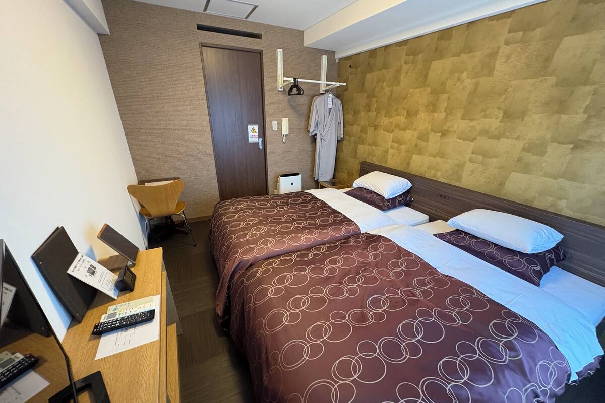 A hotel room with two beds, a desk with a computer and phone, a chair, and a wardrobe.
