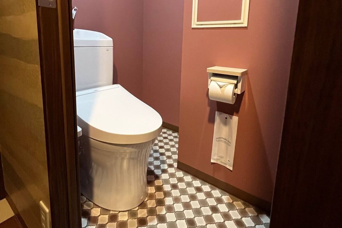 A bathroom with a toilet, a paper towel dispenser, and a checkered floor.