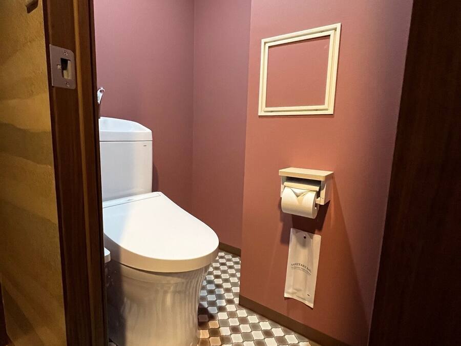 Un baño con inodoro, dispensador de toallas de papel y piso a cuadros.