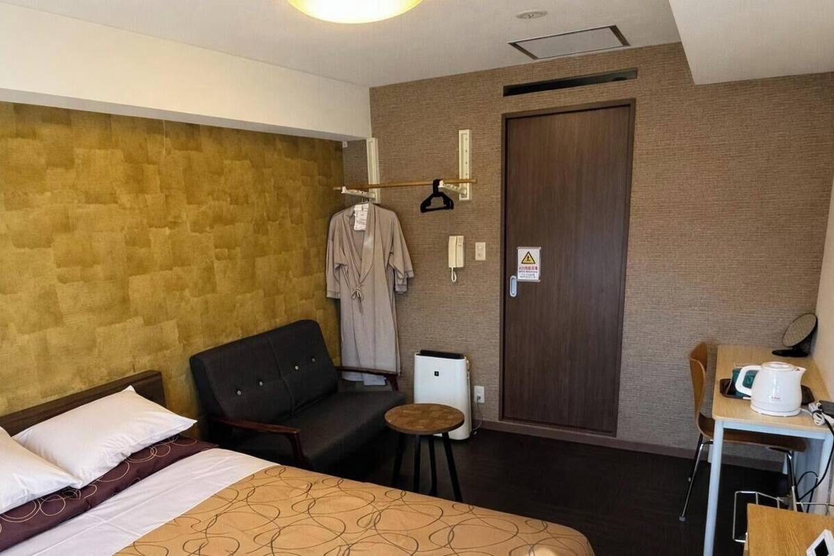 A hotel room with a bed, a chair, a small table with a kettle, and a wardrobe.