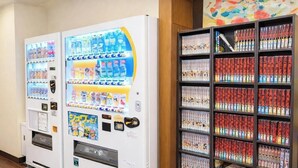 A vending machine with various drink options and a bookshelf filled with magazines. - Comfort Stay Miyabi (Chichibu)