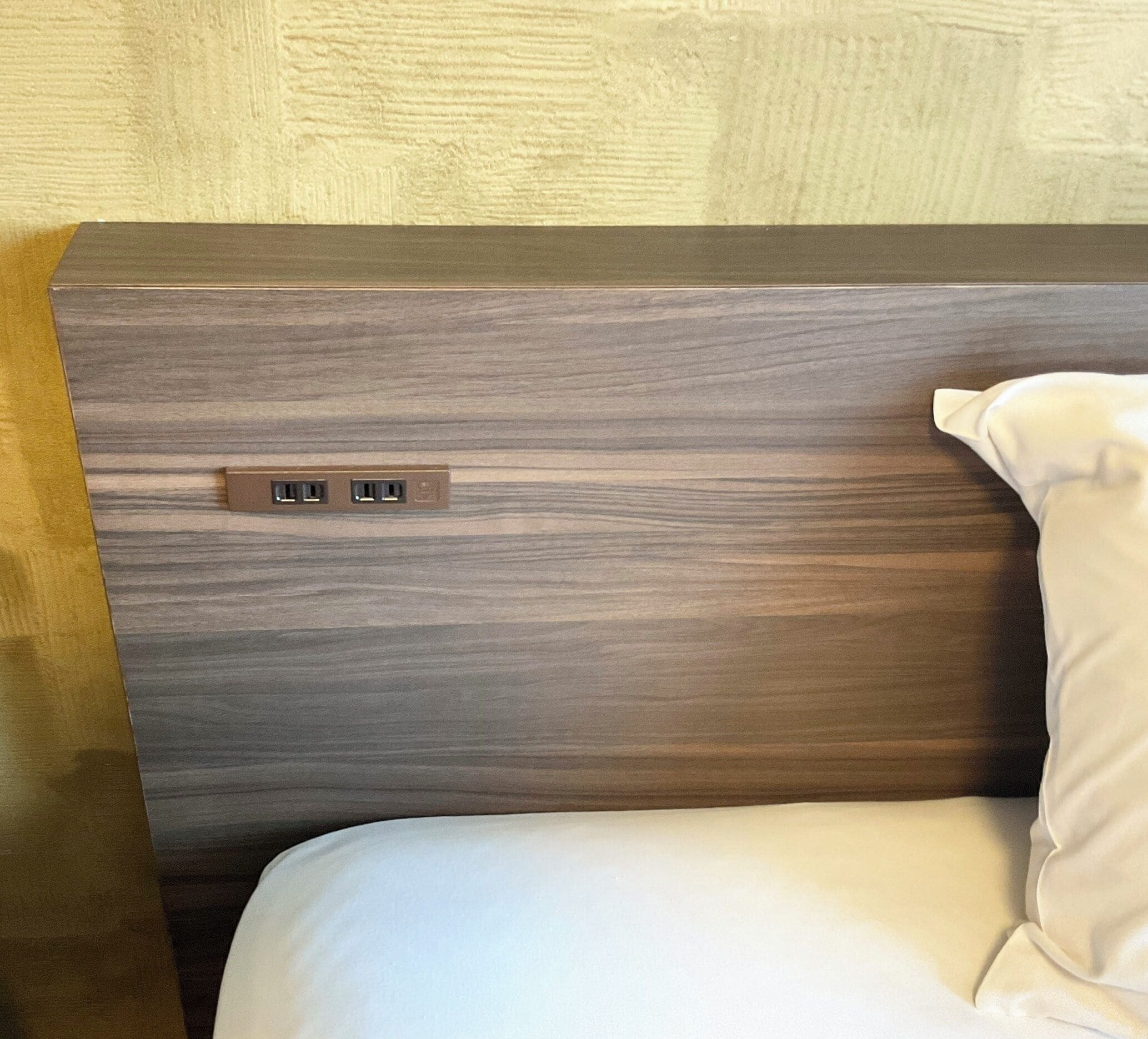 Een bed met een houten hoofdbord en een wit kussen.