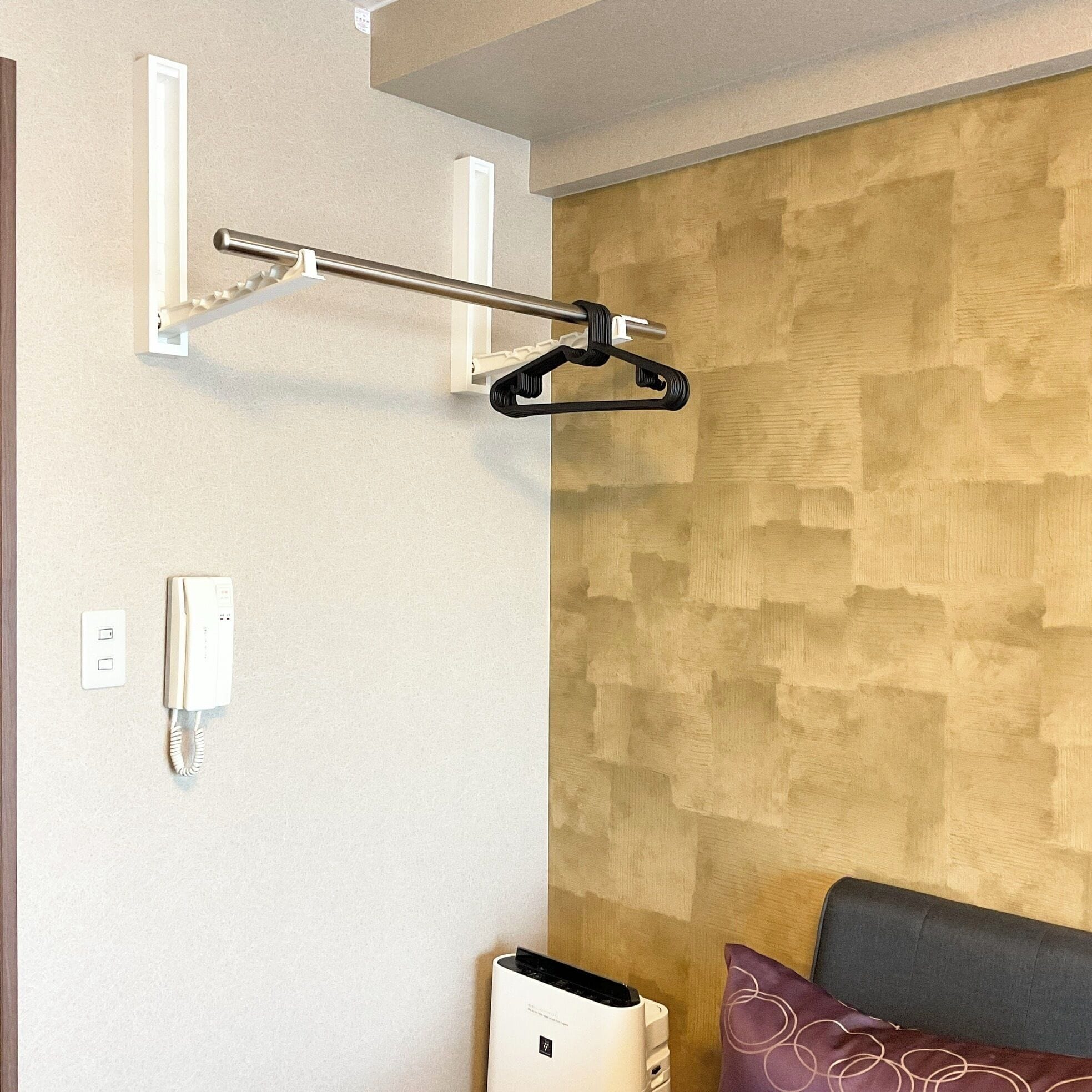 A hotel room with a wooden accent wall, a white telephone, and a black hanger on a white bracket.