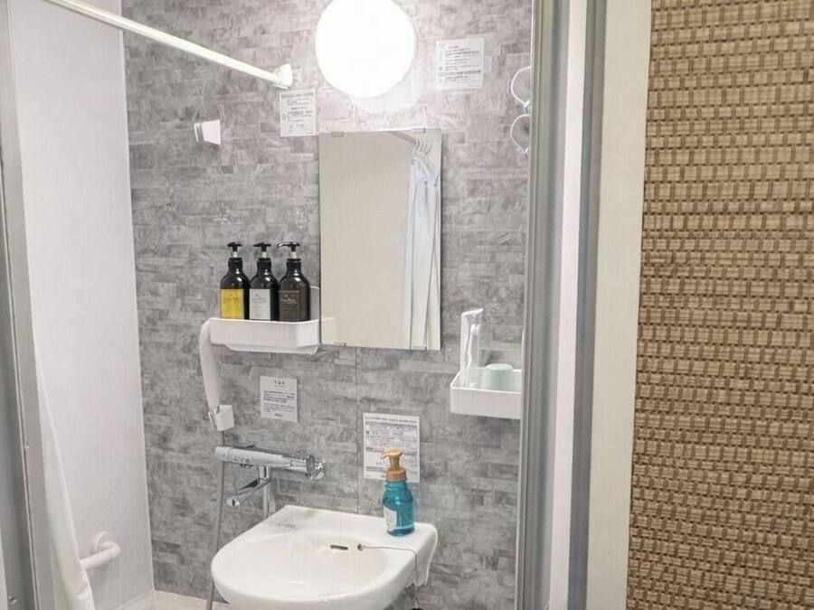 Un baño con lavamanos blanco, espejo, toallero y artículos de aseo en una repisa.