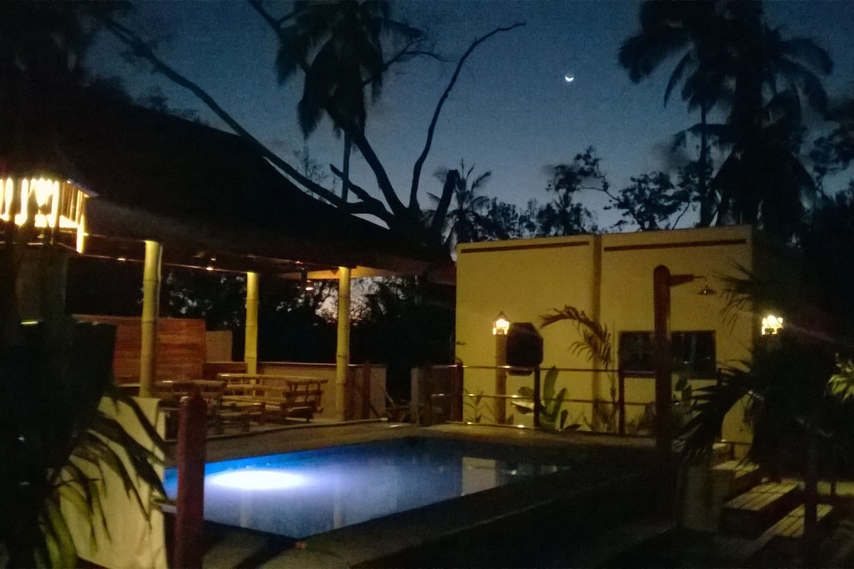 A nighttime view of a pool area with a covered seating area and a building with a flat roof.