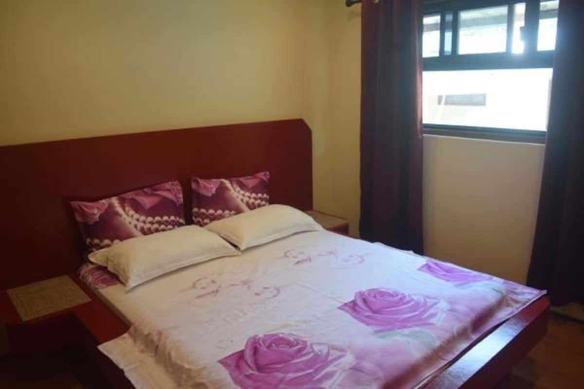 A bedroom with a bed, two pillows, a window with curtains, and a plain wall.