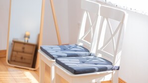Une chaise blanche avec un coussin, un plancher en bois et une fenêtre avec des stores.