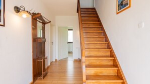 Un escalier en bois avec une rampe, une porte en bois avec un miroir et un luminaire fixé au mur.