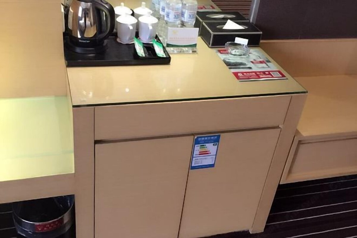 A hotel reception desk with a coffee maker, cups, and a small refrigerator.