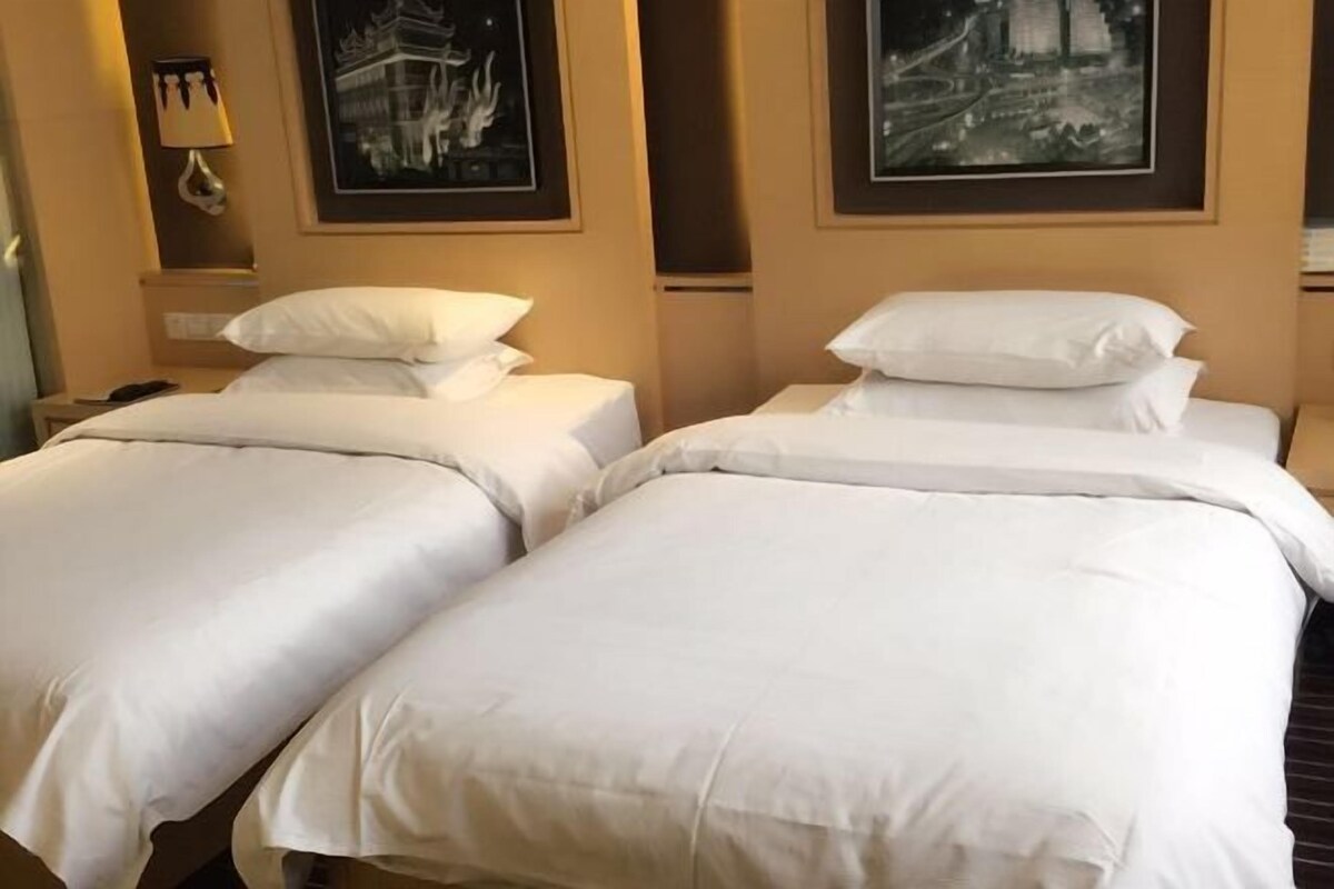 Two single beds with white linens, a bedside lamp, and framed pictures on the wall.
