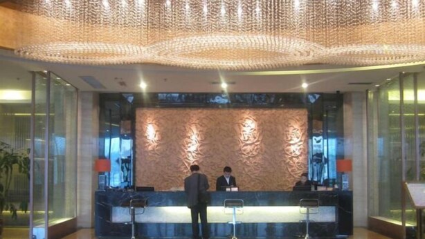 A reception area with a modern design, featuring a reception desk, two staff members, and a decorative wall. - Zhengyuan Mingyin International Hotel (Tai'an)