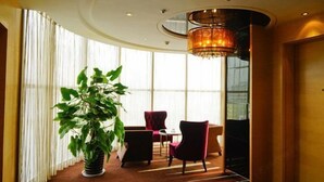 A hotel lobby with a large potted plant, red chairs, a table, and a chandelier. - Zhengyuan Mingyin International Hotel (Tai'an)