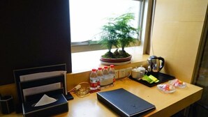 Un bureau dans une chambre d’hôtel, avec un bonsaï, un carnet noir, une bouteille d’eau, une cafetière et un plateau contenant des en-cas.